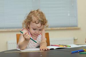 a little girl sitting at a table with a pencil photo