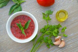 a bowl of tomato sauce with herbs and garlic on wooden desk photo