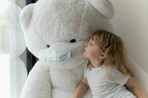 un pequeño niña es besos un grande blanco osito de peluche oso foto