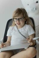 a little girl sitting in a chair with a laptop photo