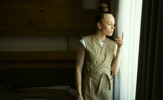 un mujer en pie en frente de un ventana con un cigarrillo foto
