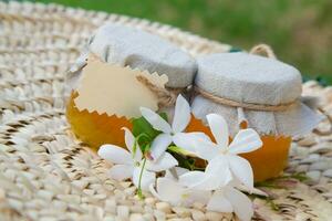 two jars of honey on a wicker table with flowers photo