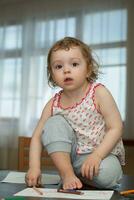 a little girl sitting on a table with a pencil photo