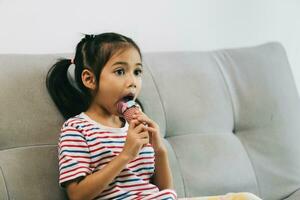 little asian girl eating ice cream on sofa in living room at home photo