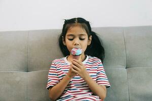 Cute little girl eating ice cream while sitting on sofa at home photo