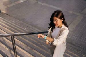 hermosa asiático mujer utilizando inteligente reloj en escalera en el ciudad foto
