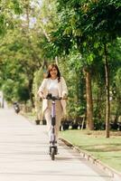asiático mujer montando eléctrico scooter en el parque, estilo de vida concepto foto