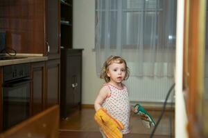 un pequeño niña en un cocina con un fregona foto