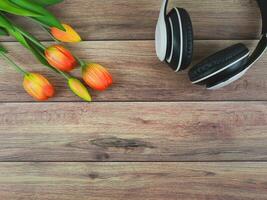white headphones and red yellow tulip flowers on wooden table background with copy space. Love song, spring music, podcast and Audio book. photo