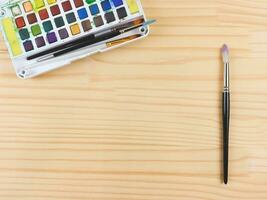 flat lay of artist workspace. Drawing tools, stationary supplies, Watercolor paints and brushes on wooden table, copy space. photo