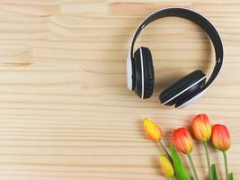 white headphones and red yellow tulip flowers on wooden table background with copy space. Love song, spring music, podcast and Audio book. photo