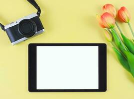 plano laico de digital tableta con blanco blanco pantalla, tulipán flores y digital cámara aislado en amarillo antecedentes. foto