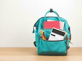 Front view  of green backpack with school supplies on wooden table and white  background with copy space. photo