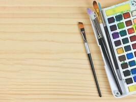 flat lay of artist workspace. Drawing tools, stationary supplies, Watercolor paints and brushes on wooden table, copy space. photo