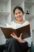 Stay home pastimes. Woman sitting in armchair with open book indoors. Beautiful young lady reading exciting story, enjoying lazy morning photo