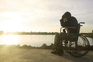 silueta joven discapacitado hombre viendo río fondo.él es aumento un mano a y sentado en silla de ruedas.desesperación,solitaria,esperanza.photo concepto depresión y paciente. foto