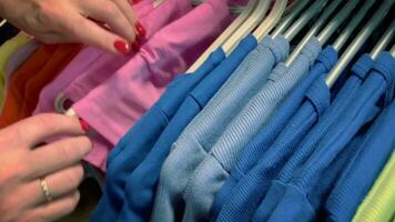 De las mujeres dedos ordenar mediante ropa colgando en perchas en el almacenar. video