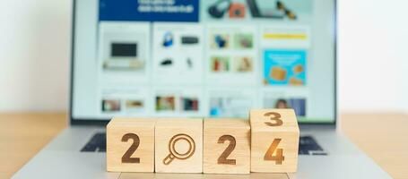 2024 block with magnifying glass icon against laptop background. Hiring, recruitment, job, jobless SEO, Search Engine Optimization and New Year concepts photo