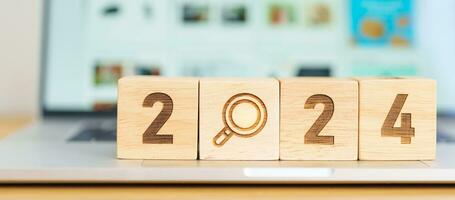 2024 block with magnifying glass icon against laptop background. Hiring, recruitment, job, jobless SEO, Search Engine Optimization and New Year concepts photo