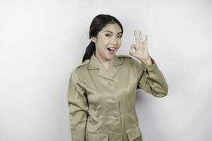 un joven asiático mujer en marrón caqui uniforme demostración Okay firmar con su dedos. indonesio gobierno obrero. foto