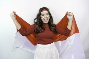 A young Asian woman with a happy successful expression wearing red top and headband while holding Indonesia's flag, isolated by white background. Indonesia's independence day concept. photo