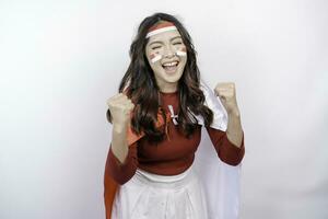 A young Asian woman with a happy successful expression wearing red top and headband while holding Indonesia's flag, isolated by white background. Indonesia's independence day concept. photo