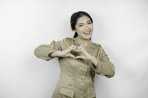 un joven asiático mujer en marrón caqui uniforme demostración oferta sensación por formación corazón con su dedos. indonesio gobierno obrero. foto