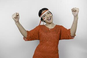 A young Asian woman with a happy successful expression wearing red kebaya and headband isolated by white background. Indonesia's independence day concept. photo