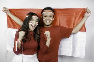 A young Asian couple with a happy successful expression wearing red top and headband while holding Indonesia's flag, isolated by white background. Indonesia's independence day concept. photo