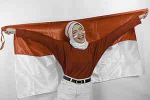 Happy smiling Indonesian muslim woman wearing red top and white hijab holding Indonesia's flag to celebrate Indonesia Independence Day. Isolated by white background. photo