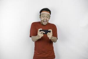 A portrait of a smiling Asian man wearing headband and holding his phone, isolated by white background. Indonesia's independence day concept photo