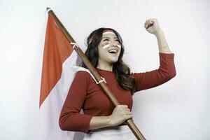 A young Asian woman with a happy successful expression wearing red top and headband while holding Indonesia's flag, isolated by white background. Indonesia's independence day concept. photo