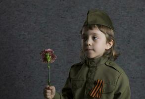 un joven chico en un militar uniforme participación un flor foto