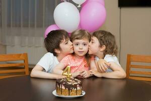 un pequeño niña besos un cumpleaños pastel foto