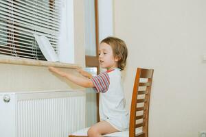 a little girl sitting on a chair near a window photo