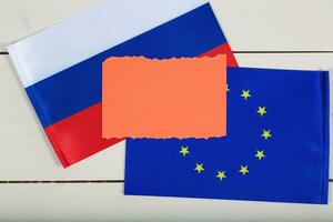 Two flags of EU and Russia on a white wooden surface. Top view photo