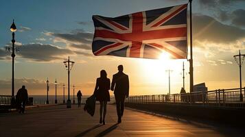 Pareja caminando debajo británico bandera en costero paseo en Inglaterra a puesta de sol. silueta concepto foto