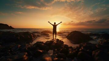 Happy man enjoying life on beach rocks by the ocean with arms wide open. silhouette concept photo