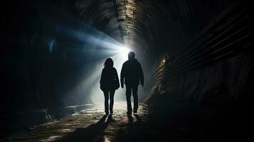 silueta Pareja caminando mediante ferrocarril túnel hacia brillante ligero a el otro final participación manos desde detrás foto