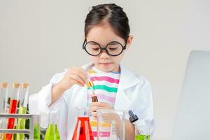 asiático pequeño niña trabajando con prueba tubo Ciencias experimentar en blanco salón de clases foto