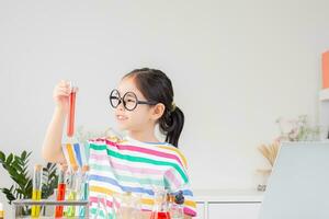 asiático pequeño niña trabajando con prueba tubo Ciencias experimentar en blanco salón de clases foto