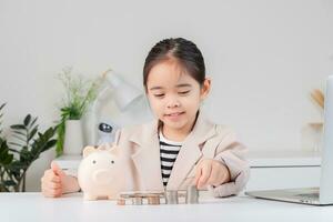 asiático pequeño linda niña vistiendo un crema traje analizando monedas Finanzas y inversión foto