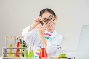 asiático pequeño niña trabajando con prueba tubo Ciencias experimentar en blanco salón de clases foto