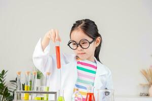 asiático pequeño niña trabajando con prueba tubo Ciencias experimentar en blanco salón de clases foto