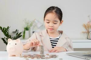 asiático pequeño linda niña vistiendo un crema traje analizando monedas Finanzas y inversión foto