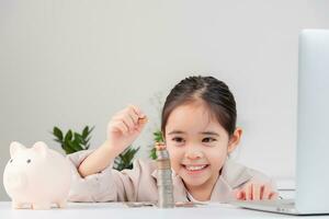 asiático pequeño linda niña vistiendo un crema traje analizando monedas Finanzas y inversión foto