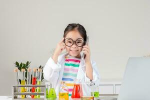 asiático pequeño niña trabajando con prueba tubo Ciencias experimentar en blanco salón de clases foto