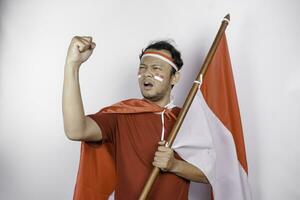 un joven asiático hombre con un contento exitoso expresión vistiendo rojo parte superior y venda mientras participación de indonesia bandera, aislado por blanco antecedentes. de indonesia independencia día concepto. foto