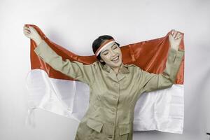 Smiling government worker woman holding Indonesia's flag isolated by white background. PNS wearing khaki uniform. Indonesia's independence day concept. photo