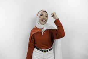 A young Asian muslim woman with a happy successful expression wearing red top and white hijab while holding Indonesia's flag, isolated by white background. Indonesia's independence day concept. photo